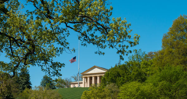 partial and distant view of Arlington House made up of columns with a US flag on a pole sitting on a hill and surrounded by trees