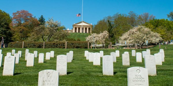 rows on grave stones in the foreground and Arlington House and flag at half mast in the background