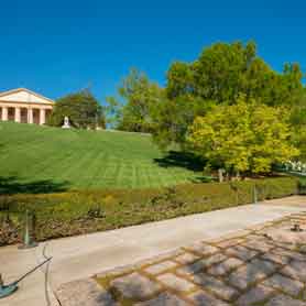 Part of John F. Kennedy Gravesite at Arlington National Cemetery showing a brick paved floor with an eternal flame and Arlington House in the background