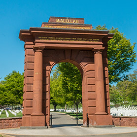 picture of a tall gate that reads 'McClellan' at the top and trees and headstones in the background