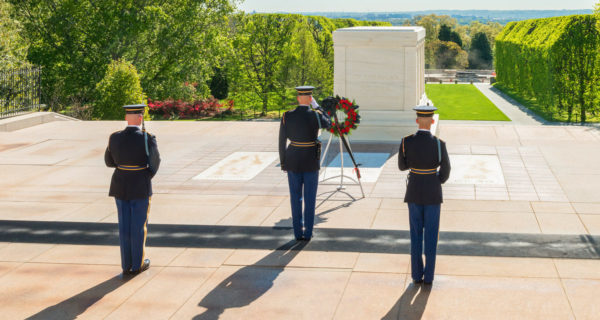 Three guards saluting and standing guard in front of a large above ground tomb dedicated to unknown soldiers at Arlington National Cemetery