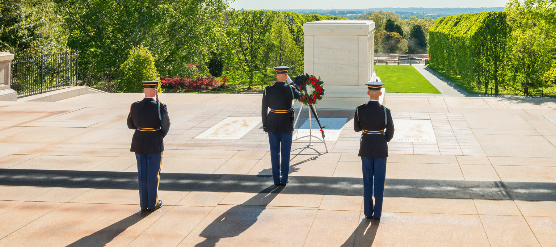 Three guards saluting and standing guard in front of a large above ground tomb dedicated to unknown soldiers at Arlington National Cemetery