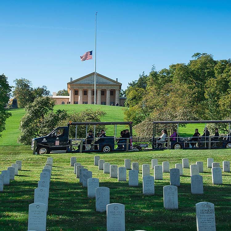 picture of arlington national cemetery vehicle driving past arlington house and tombstones in foreground